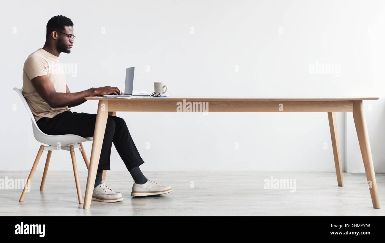 https://c8.alamy.com/comp/2HMYY96/side-view-of-focused-young-black-man-using-laptop-sitting-at-desk-working-or-studying-online-from-home-office-2HMYY96.jpg
