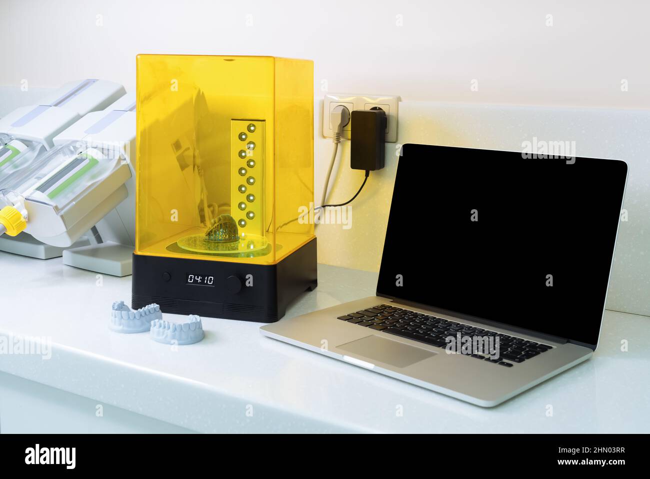 Laptop and device for washing a dental 3d print in a cleaning solution, and curing the mold using UV light. Stock Photo