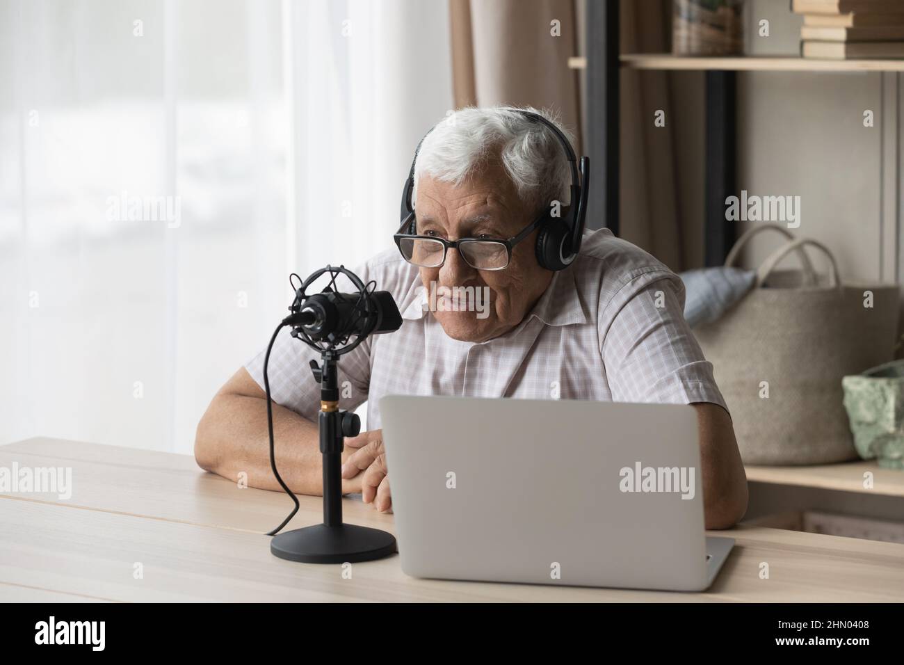 Elder radio host in headphones and glasses speaking at microphone Stock Photo