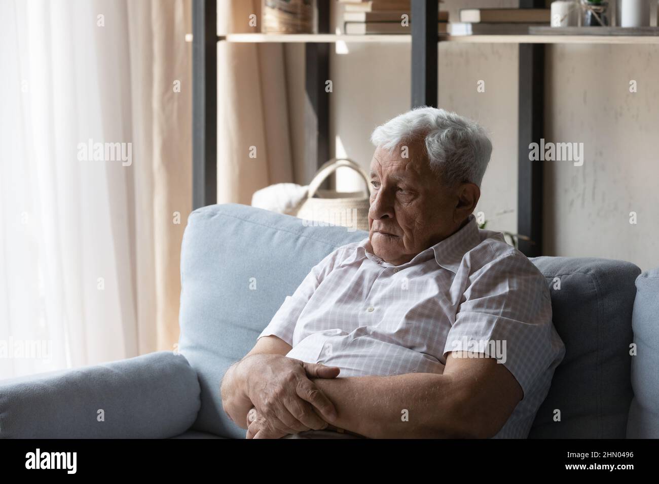 Frustrated senior elder 80s man sitting on sofa at home Stock Photo
