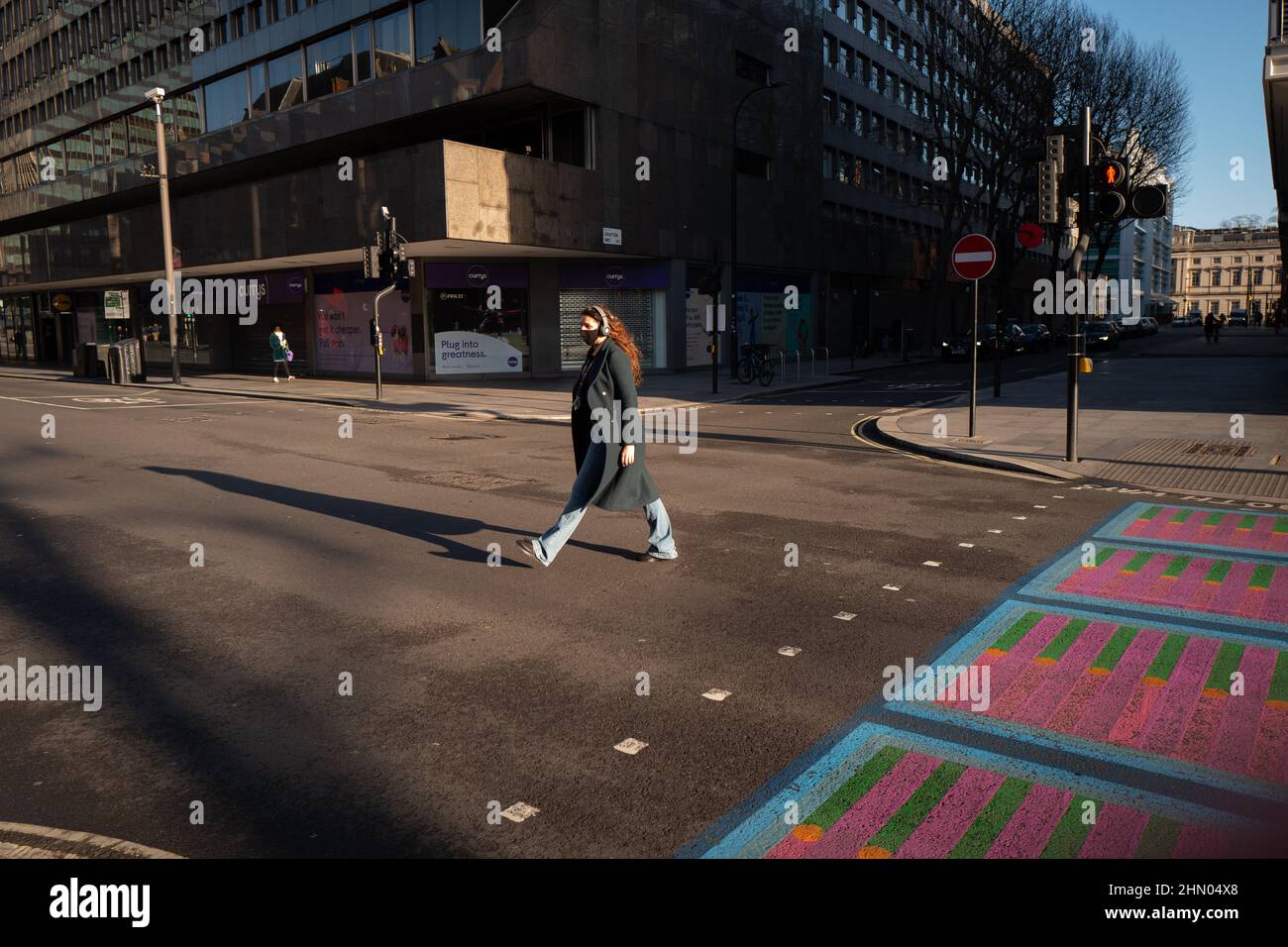 Woman with long flowing hair crosses Tottenham Court Road, London on a bright but chilly winters day. Stock Photo