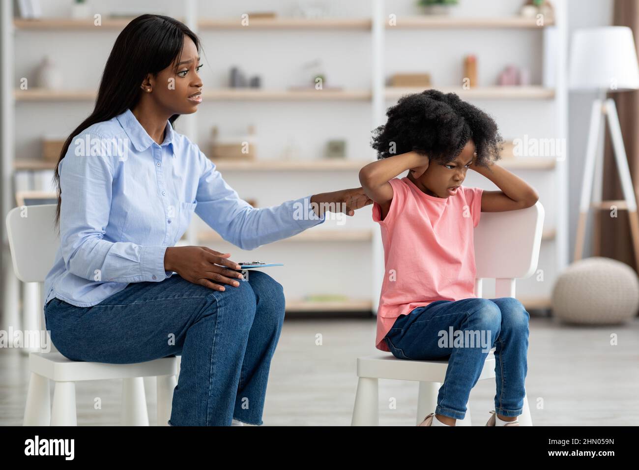 Worried black woman psychotherapist talking to unruly little girl Stock Photo
