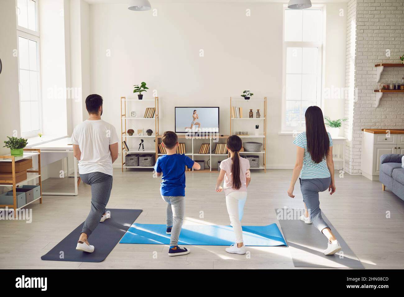 Family watching video workout on television and doing stretching exercise together Stock Photo