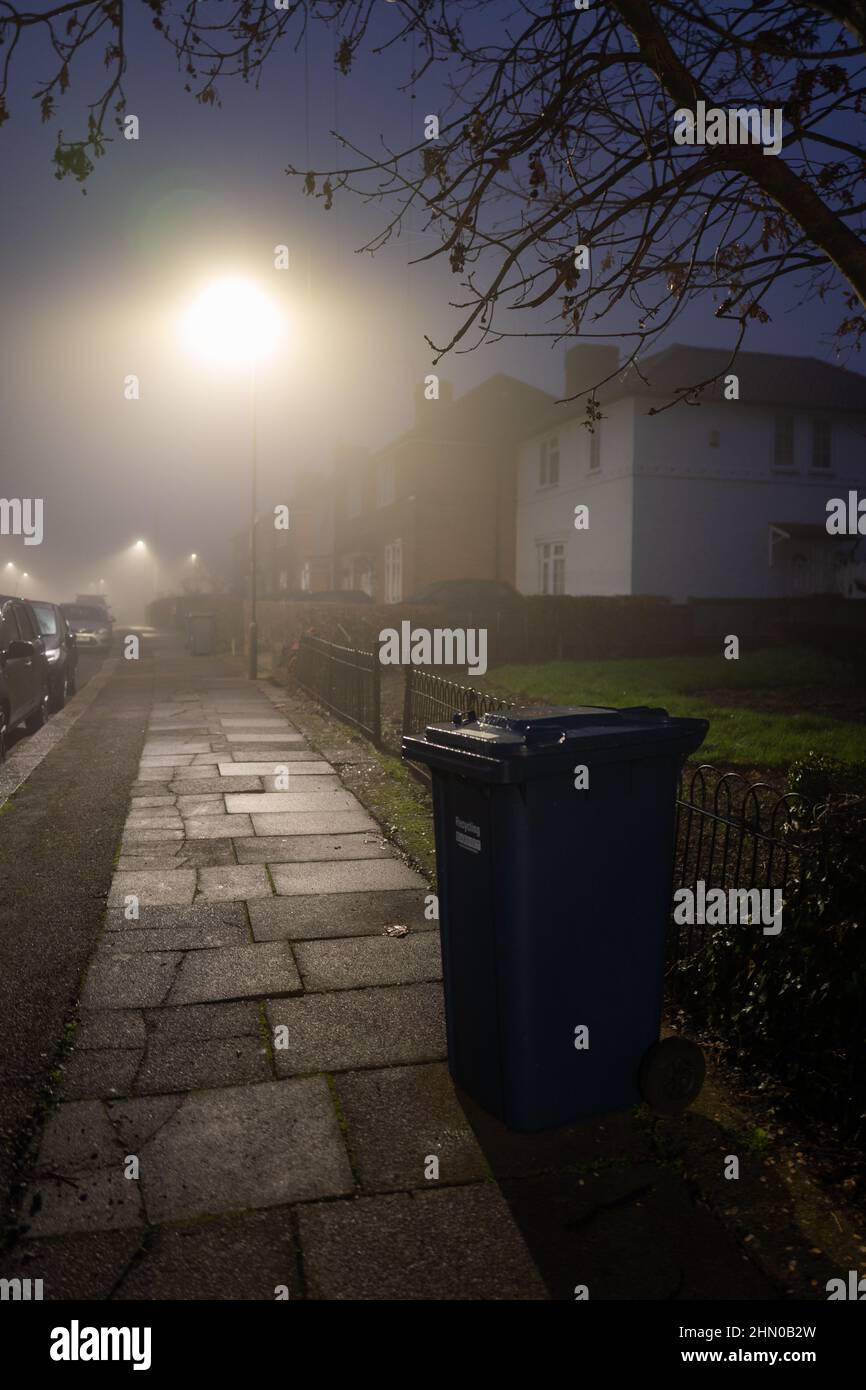 Wheelie bin under street lights on a wet foggy morning in North London, UK Stock Photo
