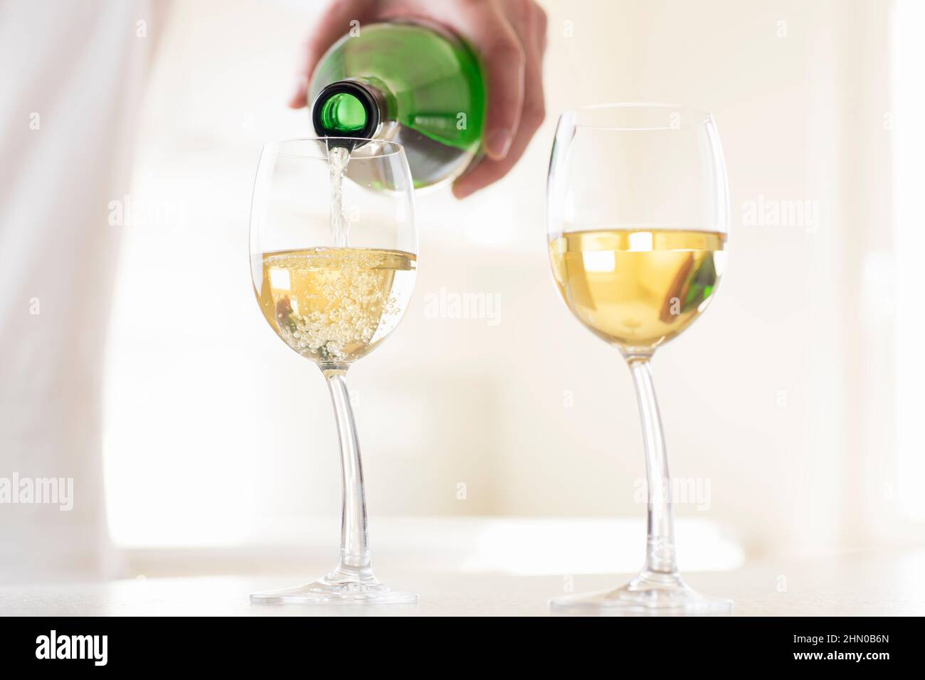 Pouring white wine into a wineglass in a white kitchen Stock Photo