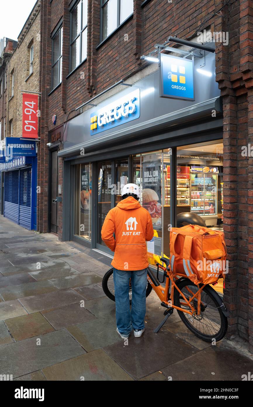 A Just Eat delivery person gets ready to enter Greggs to collect an order for delivery. Taken early on a Sunday morning in Lower Marsh,Waterloo London Stock Photo