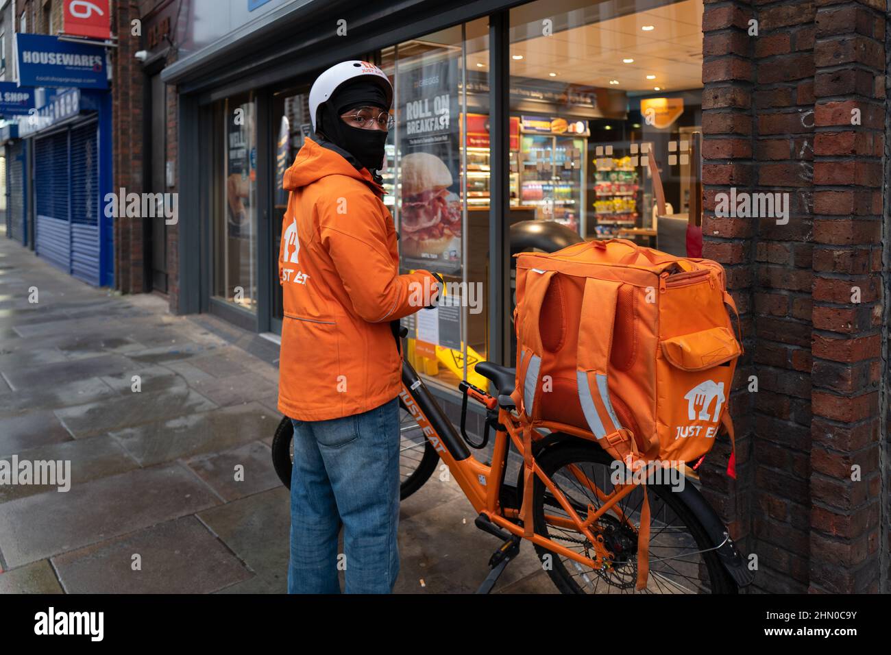 A Just Eat delivery person gets ready to enter Greggs to collect an order for delivery. Taken early on a Sunday morning in Lower Marsh,Waterloo London Stock Photo