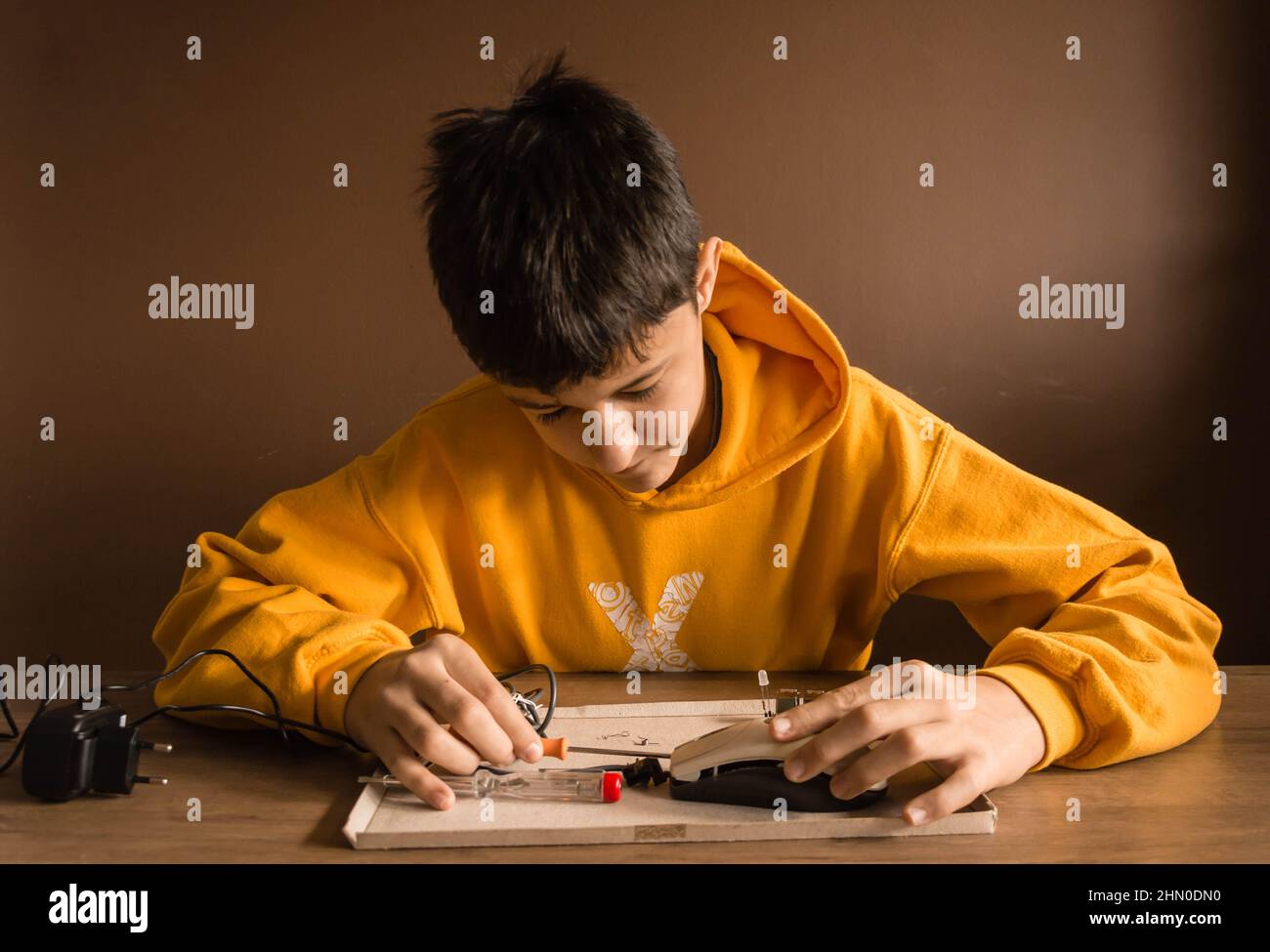 A teenage boy with brown hair is wearing a yellow hoodie. He is repairing things with tools. Stock Photo