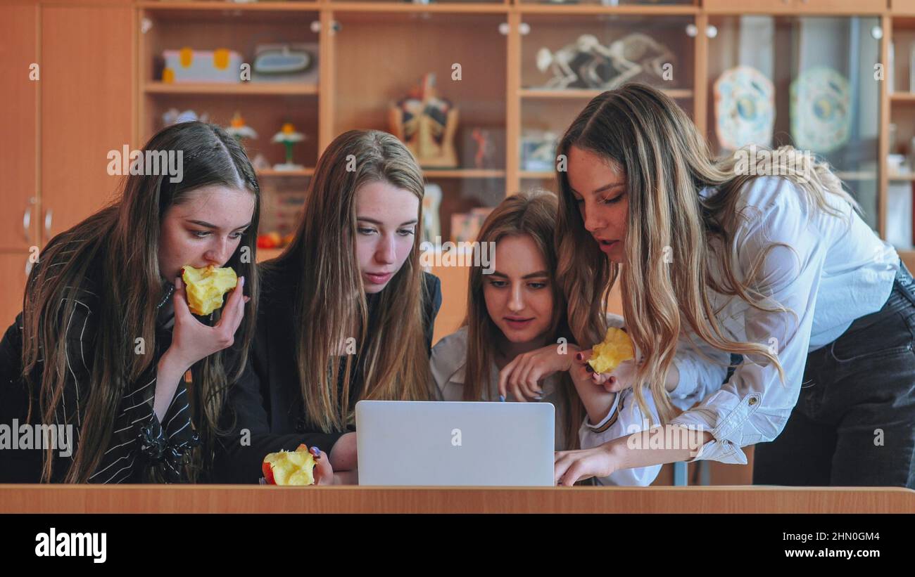Schoolgirls friends working together in class with a laptop and eating ...