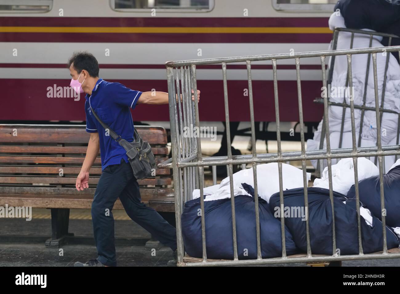 An employee at Hualamphong (Hua Lamphong) Station in Bangkok, Thailand, carting off used bedding from an overnight train Stock Photo
