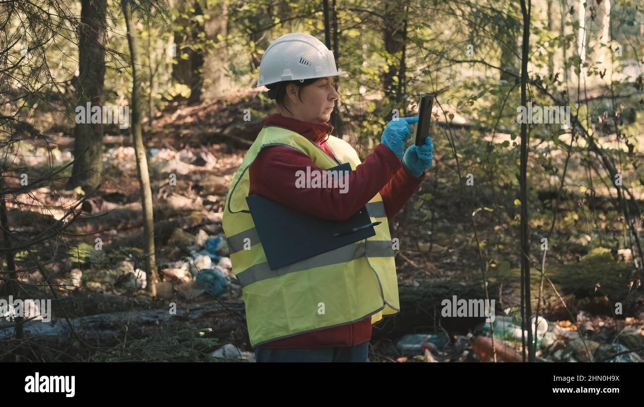 Woman environmentalist in workwear and helmet record offense - forest pollution Stock Photo