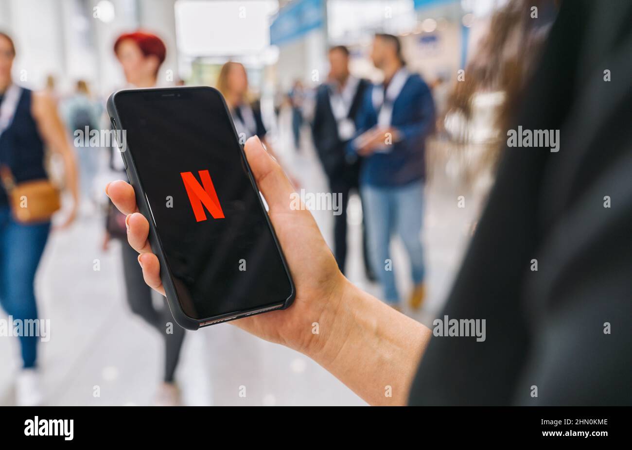 Woman hand holding iphone Xs with logo of Netflix app. Young woman is browsing the movie video library what to watch. Stock Photo