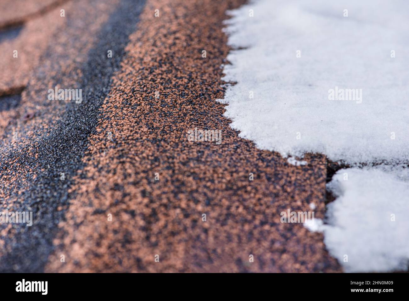 Red shingles. The roof of a house made of shingles is covered with snow in winter, close-up. Frost resistance and elasticity of bituminous tiles in Stock Photo