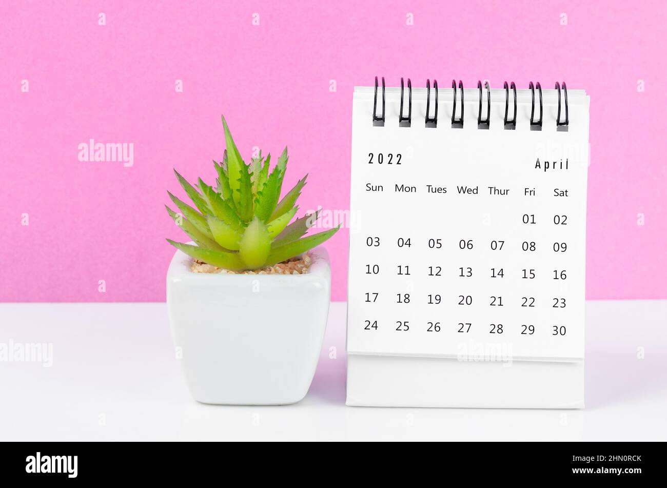 The April 2022 desk calendar with plant pot on pink background. Stock Photo