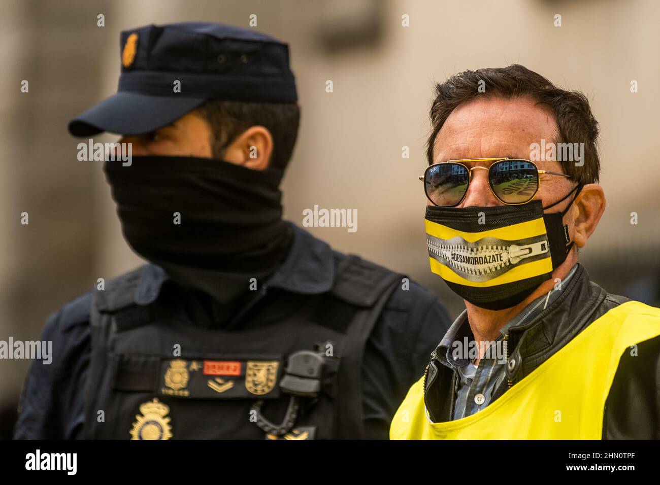 Madrid, Spain. 13th Feb, 2022. A man with the word 'ungag' on his face mask is seen near a police officer during a demonstration against the Citizen Security Law known as Gag Law (Ley Mordaza). The citizen platform 'No Somos Delito', together with groups, organizations and social movements that work for the defense of Human Rights, have called for a demonstration to demand that the reform of the Gag Law proposed by Government respond to some minimums that guarantee the free exercise of fundamental rights. Credit: Marcos del Mazo/Alamy Live News Stock Photo