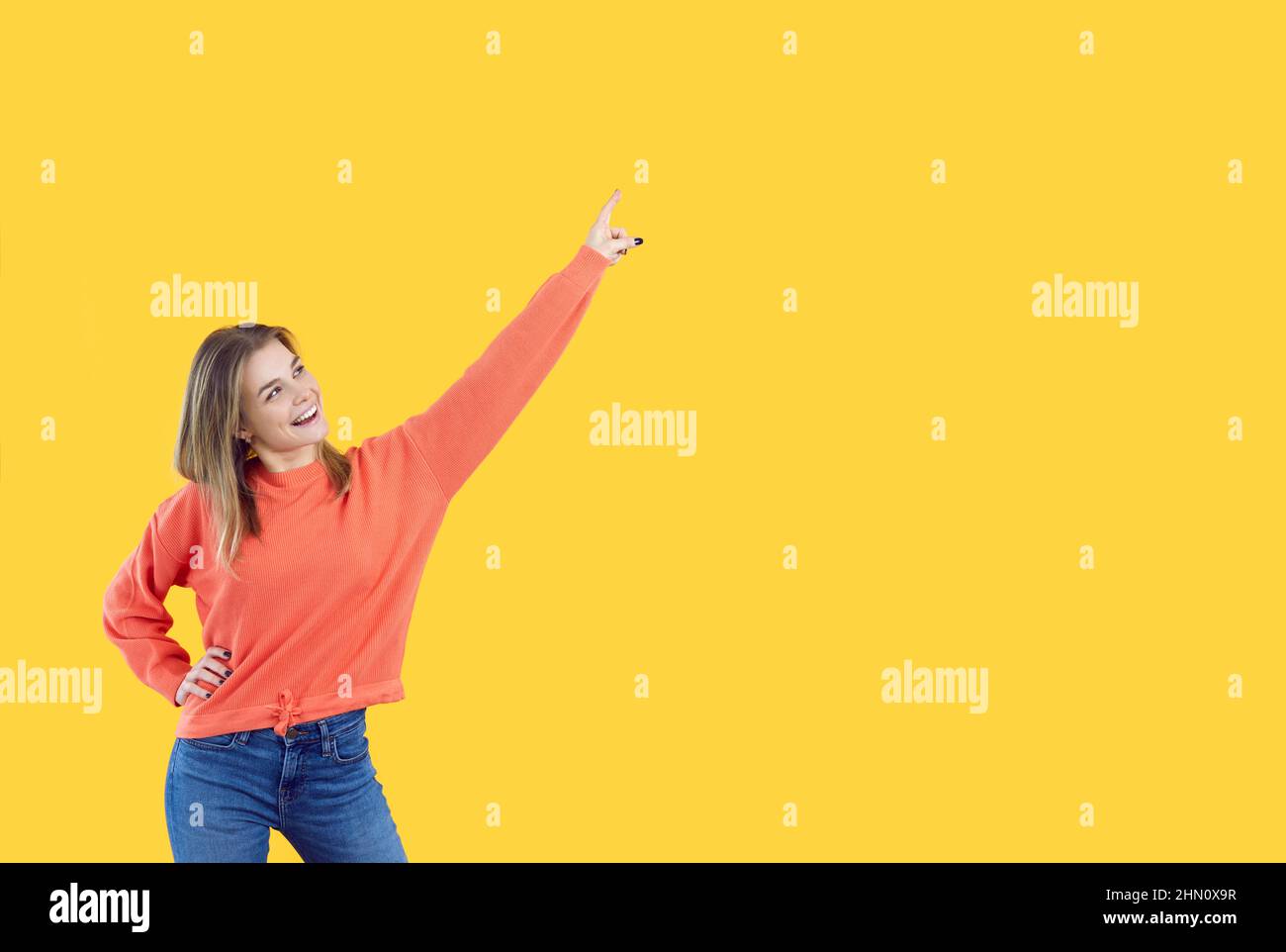 Happy young girl looking up, smiling and pointing her finger at copy space background Stock Photo