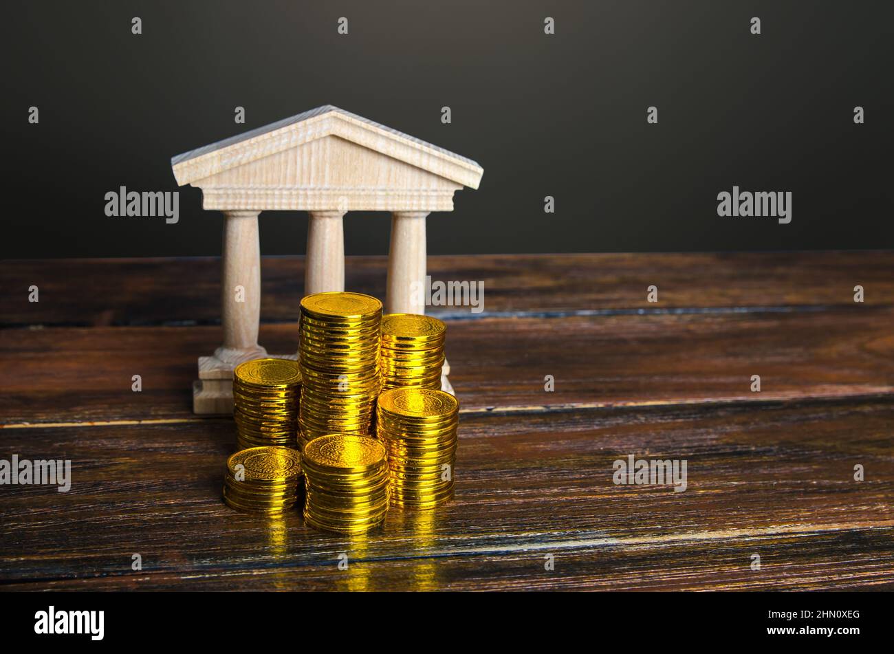 Bank building and coins stacks. State debt. Budget. Tax collection. Investments in education, museums and libraries, government institutions. Bank cap Stock Photo