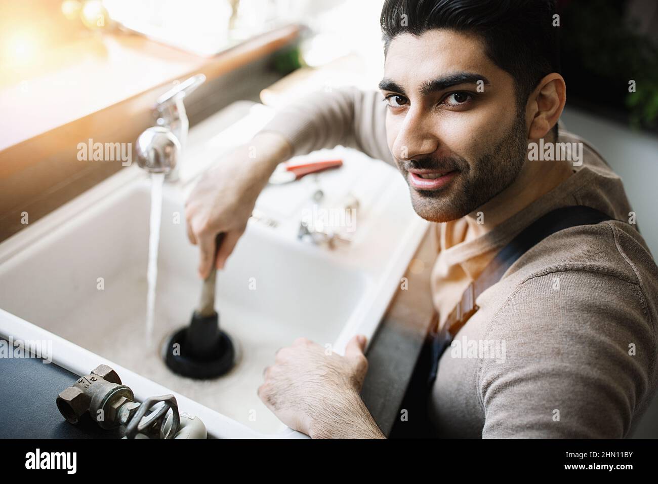 Handyman at work. Repairing kitchen sink by plunger. man trying to fix kitchen sink. Stock Photo
