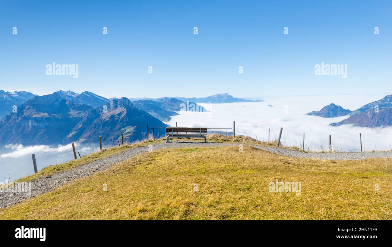 Bench on top of the mountain. Grandiose panorama of mountains and clouds from the top. Stock Photo