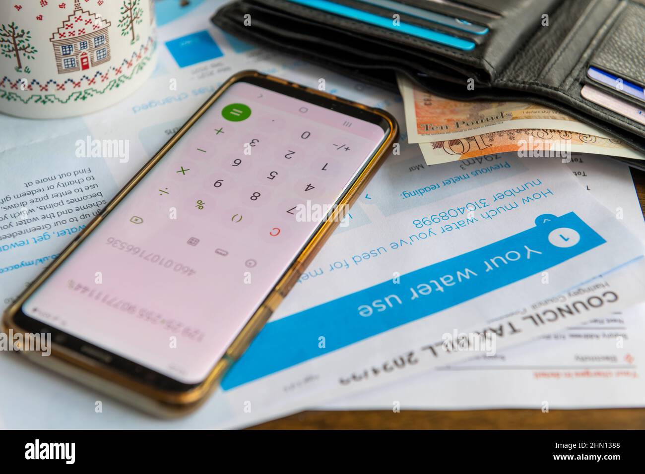 Utility and tax bills on a table with a mug of tea, phone calculator and an open purse with some bank notes. Inflation, raising cost of living concept Stock Photo