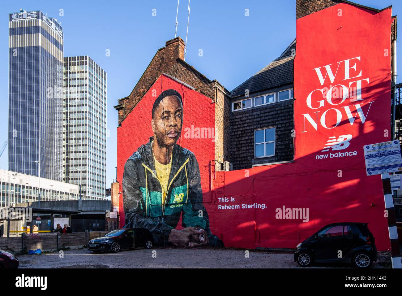A large advertising mural on a building wall next to a car park in the Northern Quarter of Manchester with the iconic CIS tower building. Stock Photo