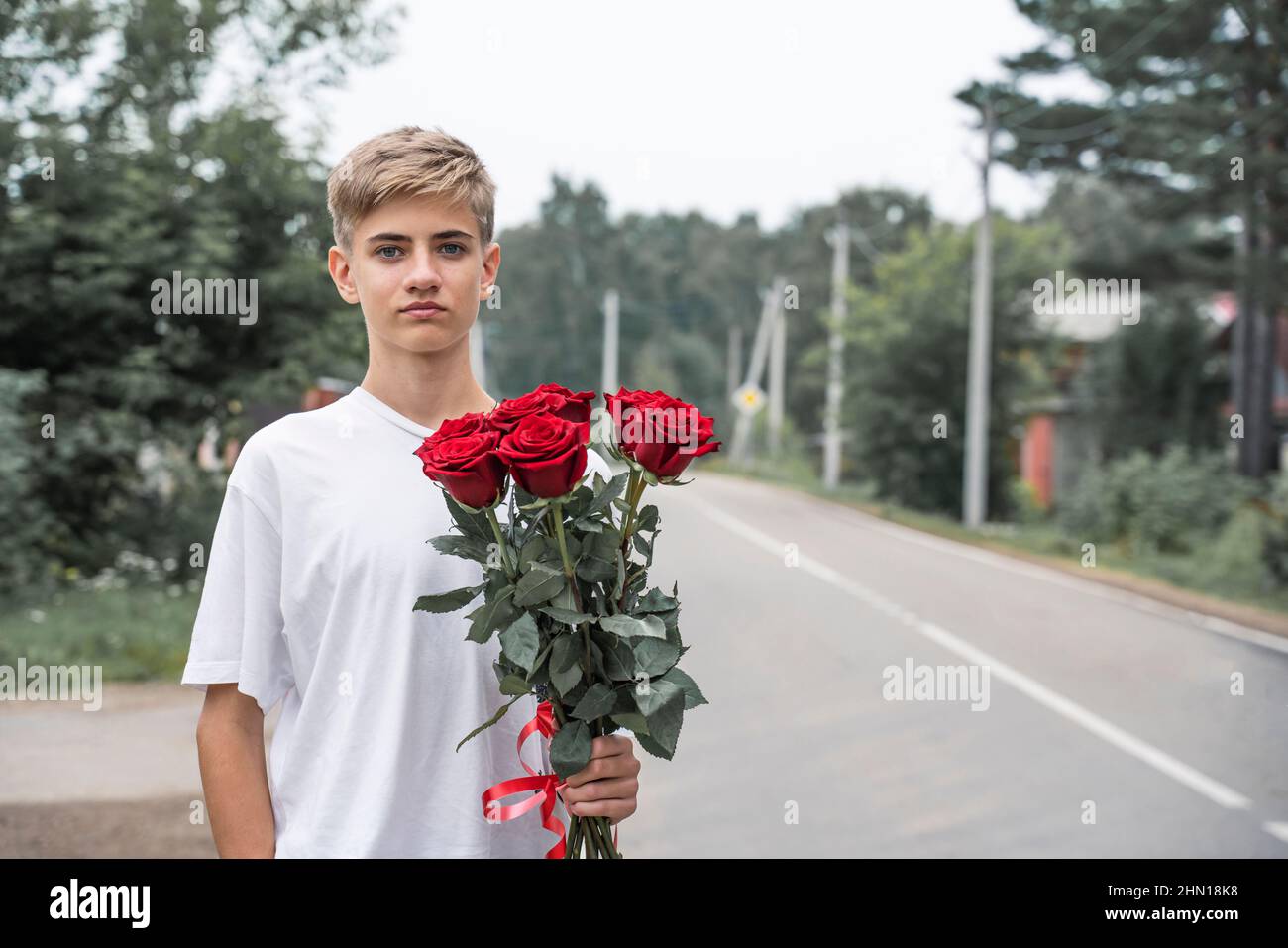 Posh boy with flowers on a natural background. Charming teenager with a bouquet of roses.  Stock Photo
