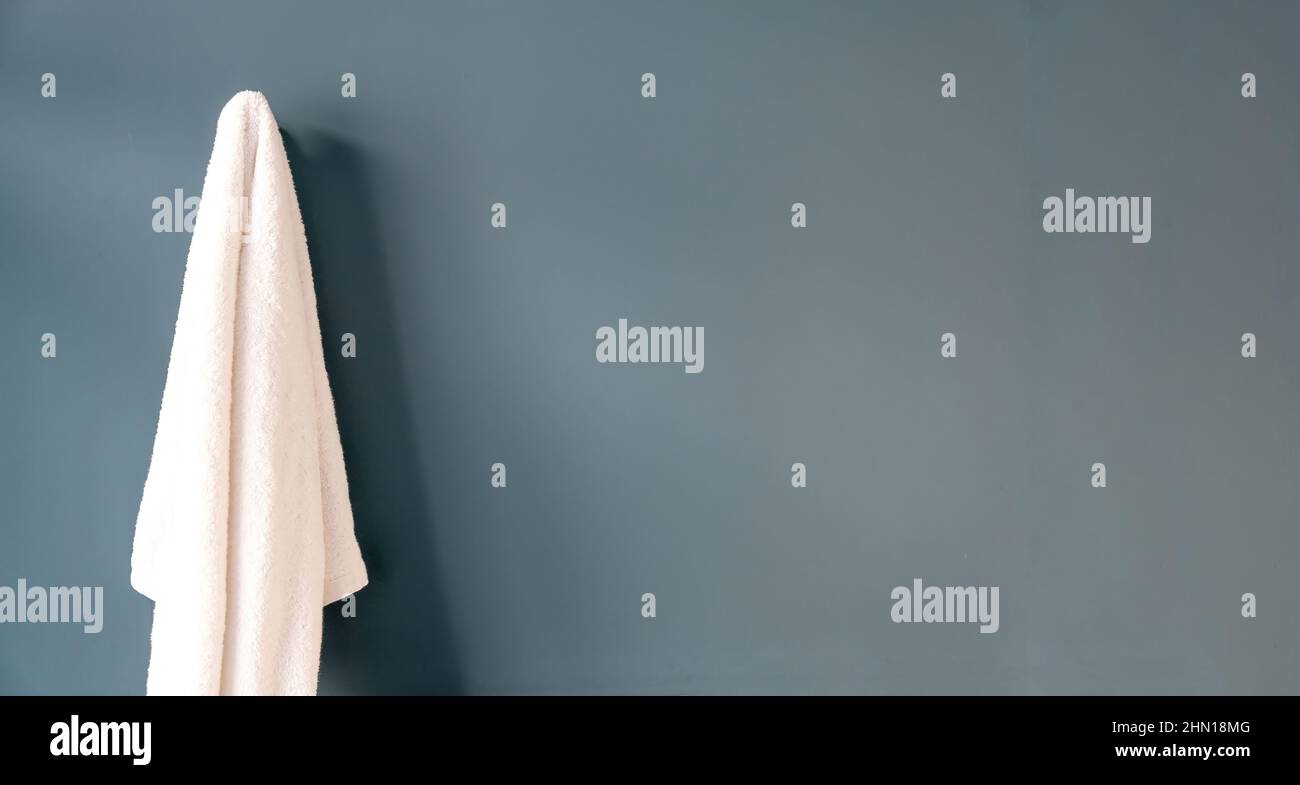 White bath towel hanging on a hook, blue bathroom wall background