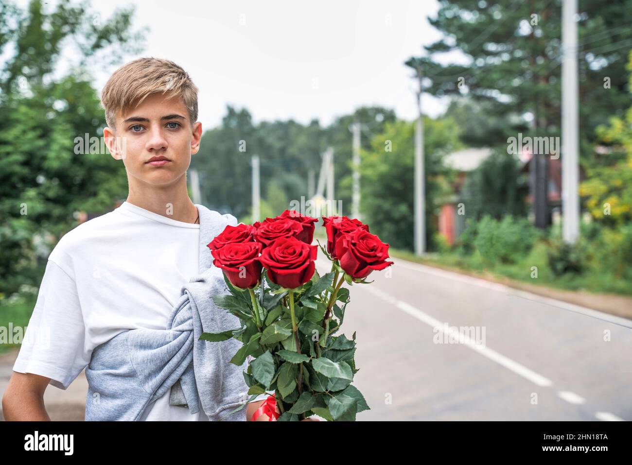 Handsome teenager holds a bouquet of red roses in his hands. Student, high school student, Romantic. Stock Photo