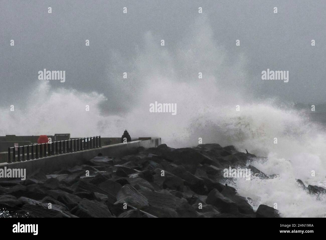 West Bay Dorset, UK.  13th February 2022.  UK Weather.  A thrill seeking walker gets close to the waves from the stormy seas which are crashing against the sea defences at West Bay in Dorset on an afternoon of heavy rain and gale force winds.  Picture Credit: Graham Hunt/Alamy Live News Stock Photo