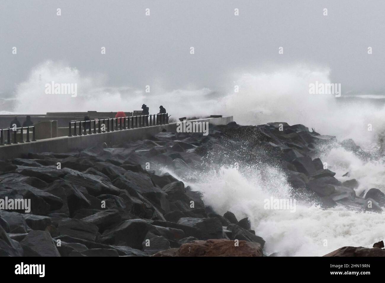 West Bay Dorset, UK.  13th February 2022.  UK Weather.  Thrill seeking walkers gets close to the waves from the stormy seas which are crashing against the sea defences at West Bay in Dorset on an afternoon of heavy rain and gale force winds.  Picture Credit: Graham Hunt/Alamy Live News Stock Photo