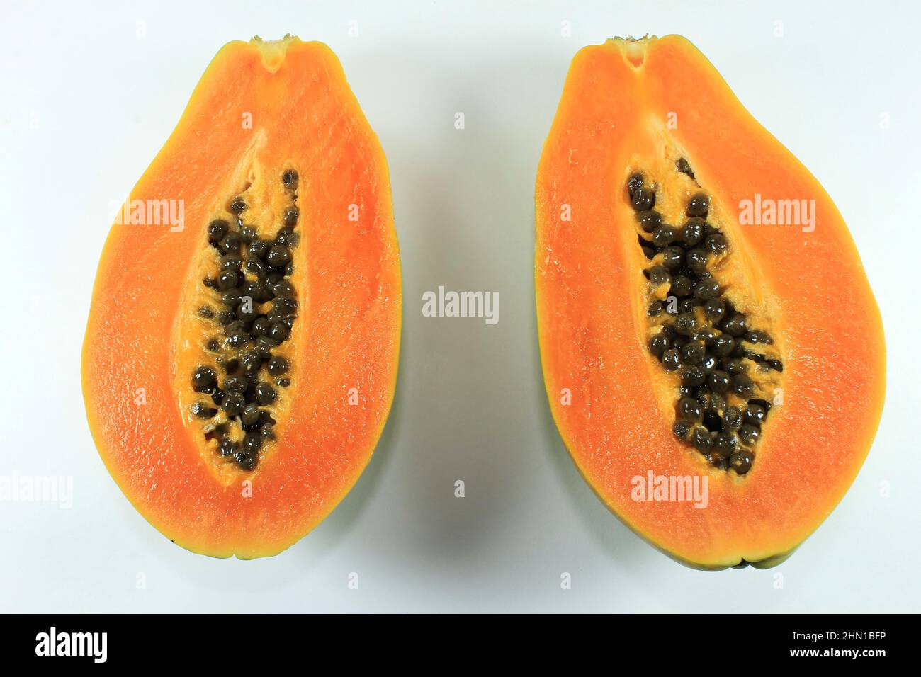 The papaya fruit cut in half with its seeds, over white background
