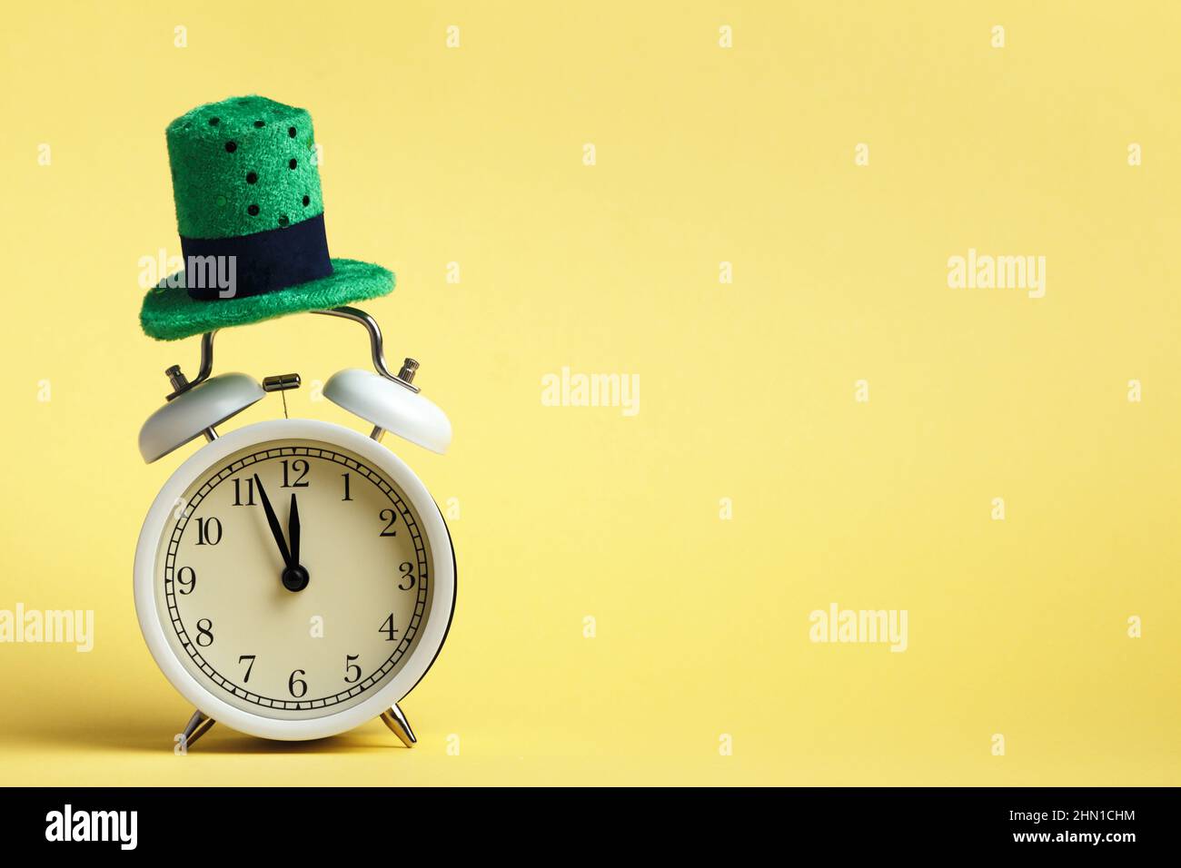 St. Patricks Day celebration concept. Alarm clock in a green hat on a yellow background. Stock Photo