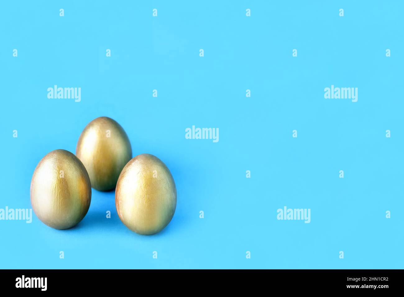 Easter eggs on blue background. Three golden eggs. Minimal style. Easter decorations. Stock Photo