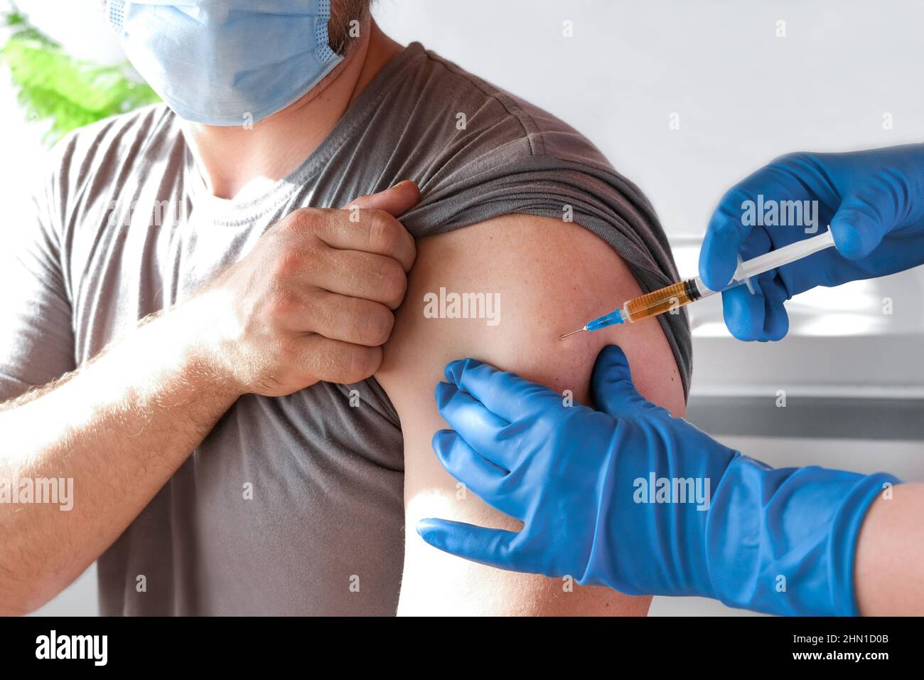 Hands of doctor injecting coronavirus covid-19 vaccine in vaccine syringe to arm muscle of caucasian man for covid immunization. Stock Photo