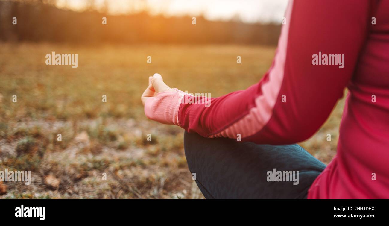 Back view of woman hands sitting in yoga lotus pose outdoor at sunrise, meditation for balance. Horizontal banner with copy space for text. Stock Photo