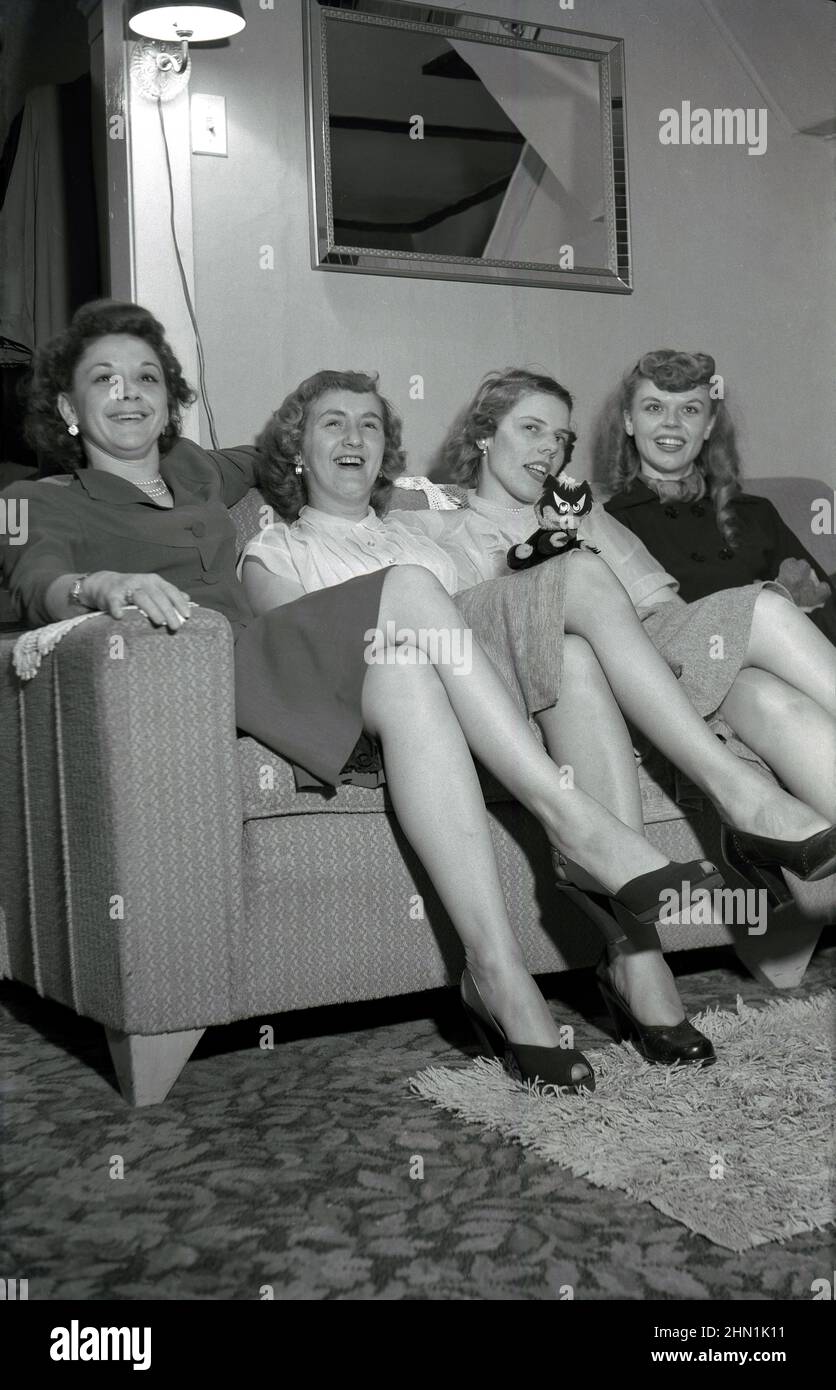 1950s, historical, inside a room, at a party, four ladies, two mothers and their daughers sitting beside each other on a sofa, smile for the camera showing some their shapely legs, USA. Stock Photo