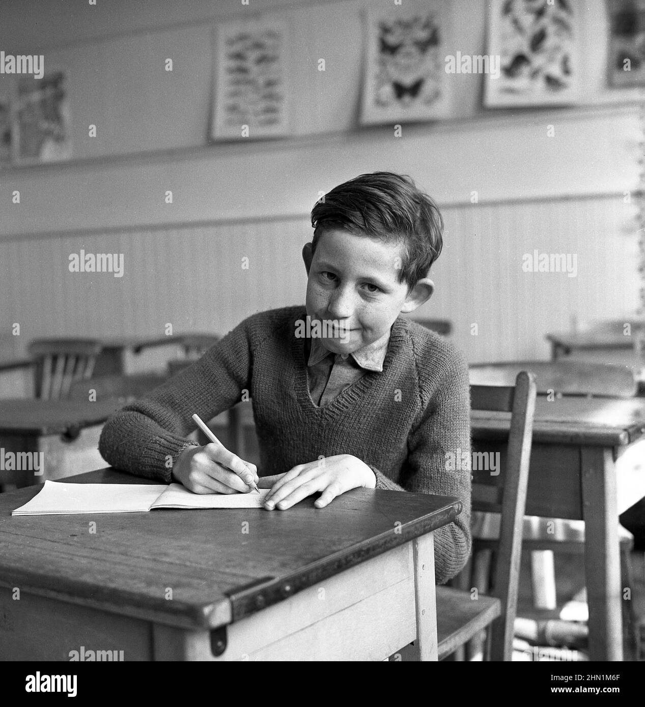 1960s, historical, young school boy, on his own in a classroom, sitting at a traditional school desk writing in his notebook, Crombie School, Fife, Scotland, UK. Stock Photo