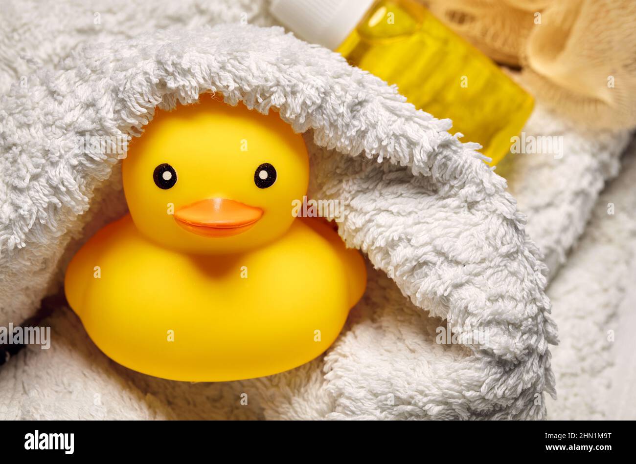 Yellow rubber duck toy wrapped in a white towel in the bathroom. Baby
