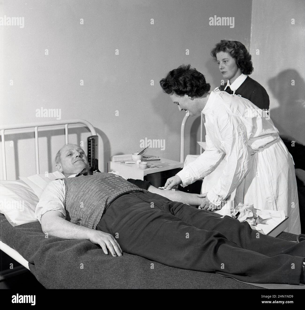 1950s, historical, a male steel worker lying on a metal bed having a blood test done by a factory nurse, Wales, England, UK. Stock Photo