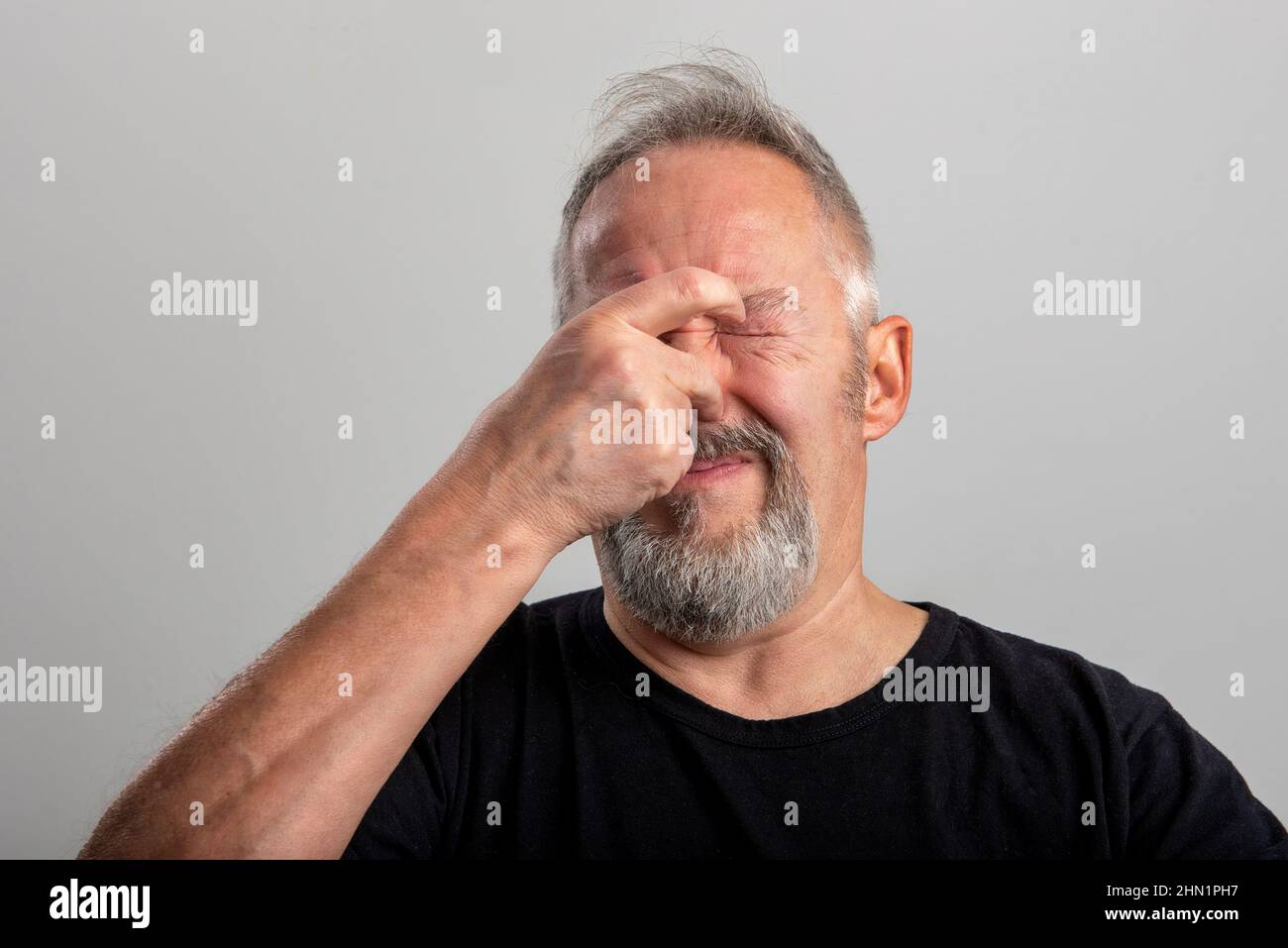 the middle-aged man holds his hand firmly on his nose to plug the horrible smell he is smelling. Isolated on gray background with space for your copy Stock Photo