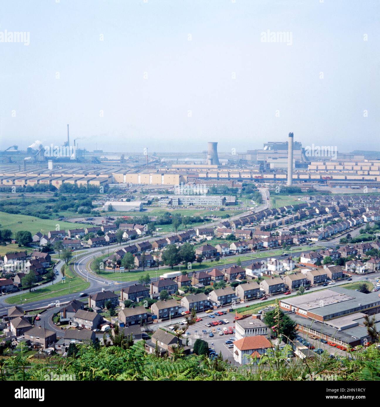 A view of the Port Talbot Steelworks, an integrated steel production plant in Port Talbot, West Glamorgan, Wales, UK c. 1980. The main access road at this time was Cefn Gwrgan Road, here running from the bottom left over a railway bridge to the works. This access road was cut by the building of Harbour Way bypass in 2013. This image is from a vintage colour transparency – a vintage 1970s/80s photograph. Stock Photo