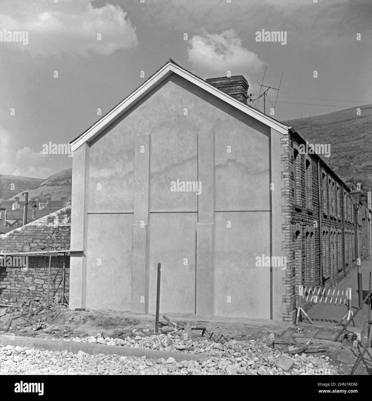 The building of Central Road (running left to right in the foreground), Port Talbot, West Glamorgan, Wales, UK in the late 1950s – here the new road had required the demolition of terraced houses. A new concrete end wall (or gable end with buttressing) was added to 16 Penrhyn Street. Central Road was one of the main access routes to the steelworks. Eventually the main route to the works was via Cefn Gwrgan Road. However, both these access roads were cut by the building of Harbour Way bypass in 2013 – a vintage 1950s/60s photograph. Stock Photo