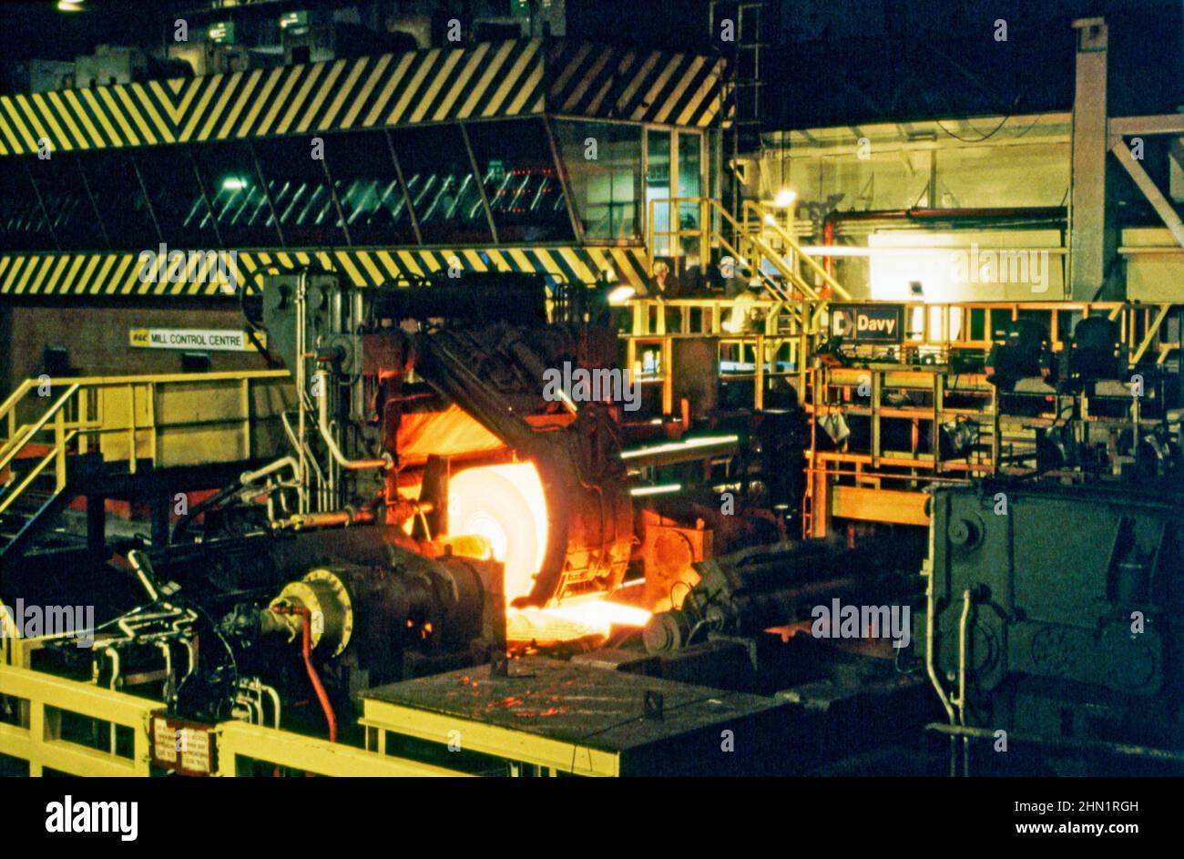 A mid-1980s view inside the Port Talbot Steelworks, an integrated steel production plant in Port Talbot, West Glamorgan, Wales, UK. Inside the mill hot sheet-steel is being rolled out on the production line. The Mill Control Centre is in the background. This image is from a vintage colour transparency – a vintage 1980s photograph. Stock Photo