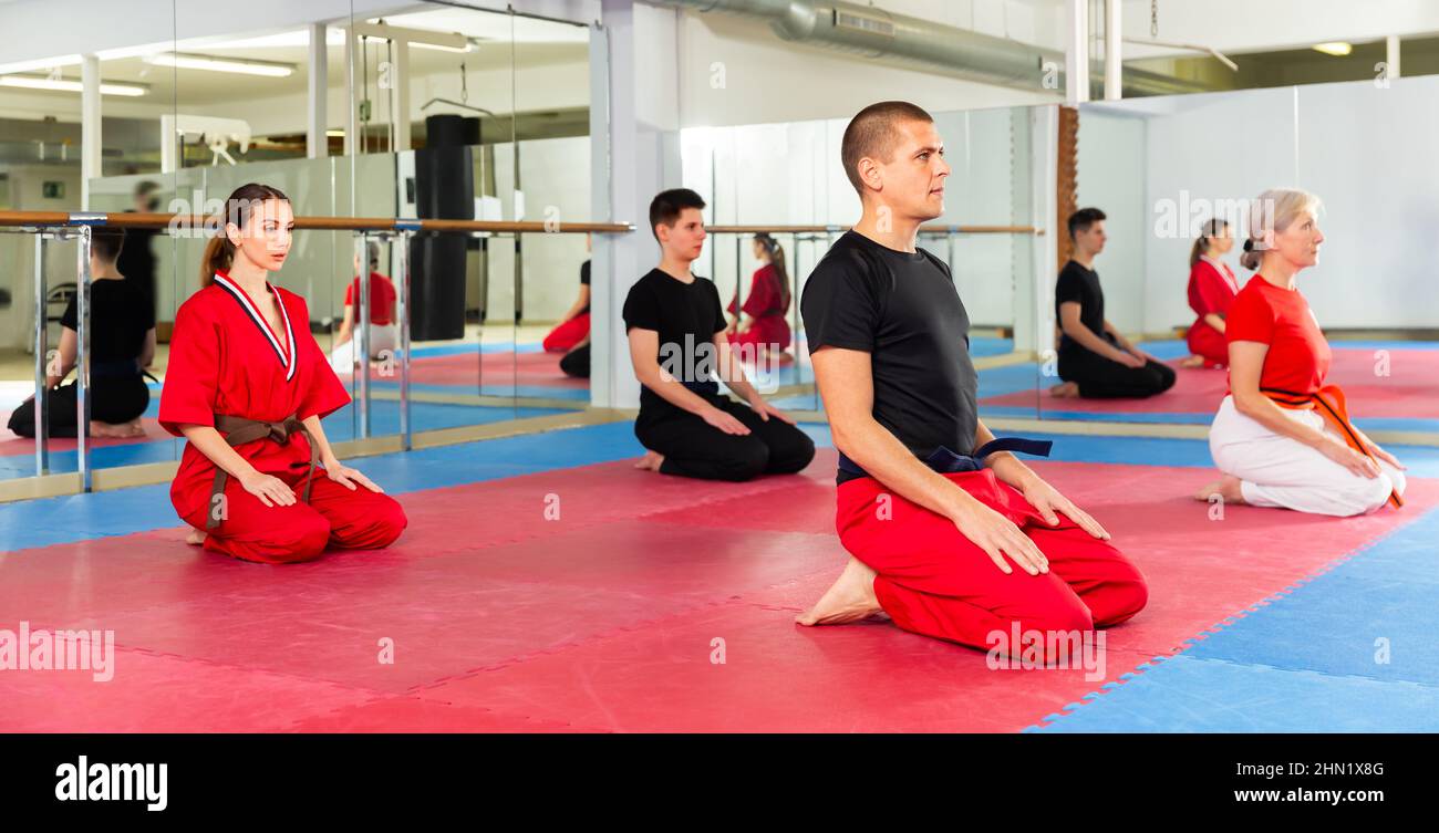 Man in red and black martial arts uniform sitting on mat in gym Stock