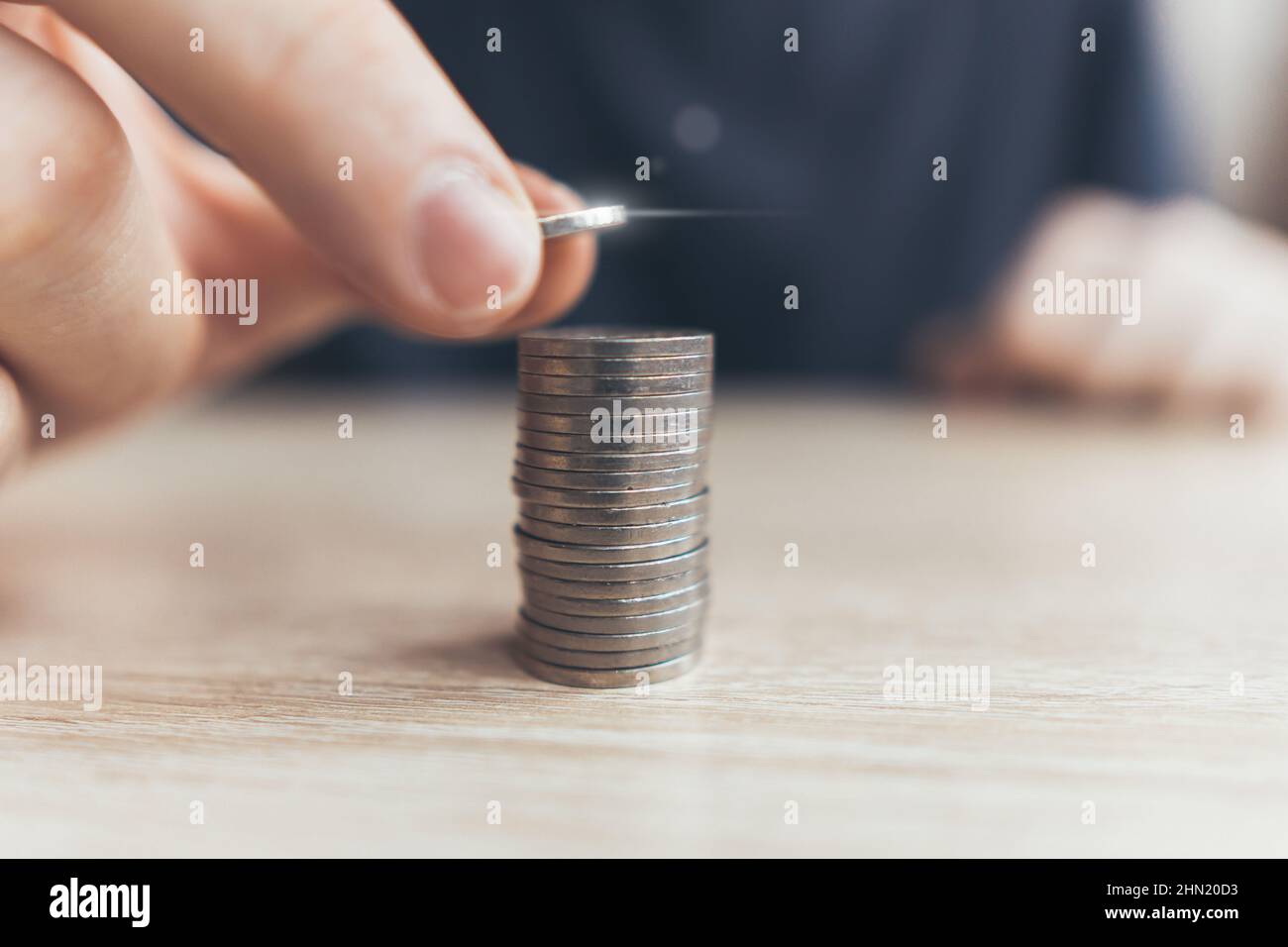 The person puts the coins into a stack of money. The concept of capitalization and investment. Stock Photo