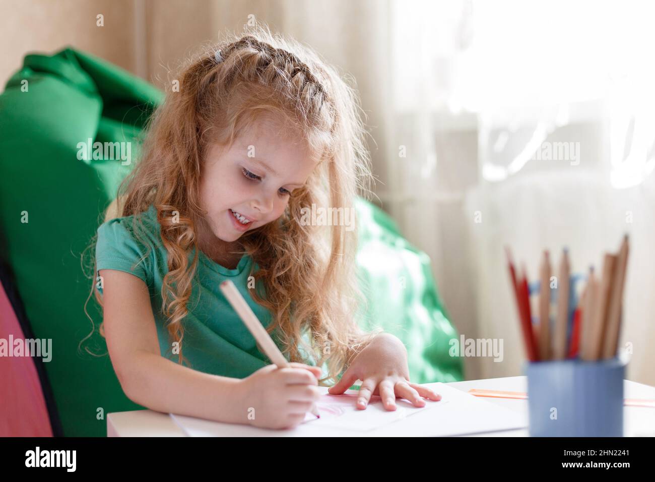 Little girl child kid in children's room play draws with interest by pencils in nursery. 5 Years happy smiling preschool baby girl draws in room alone Stock Photo