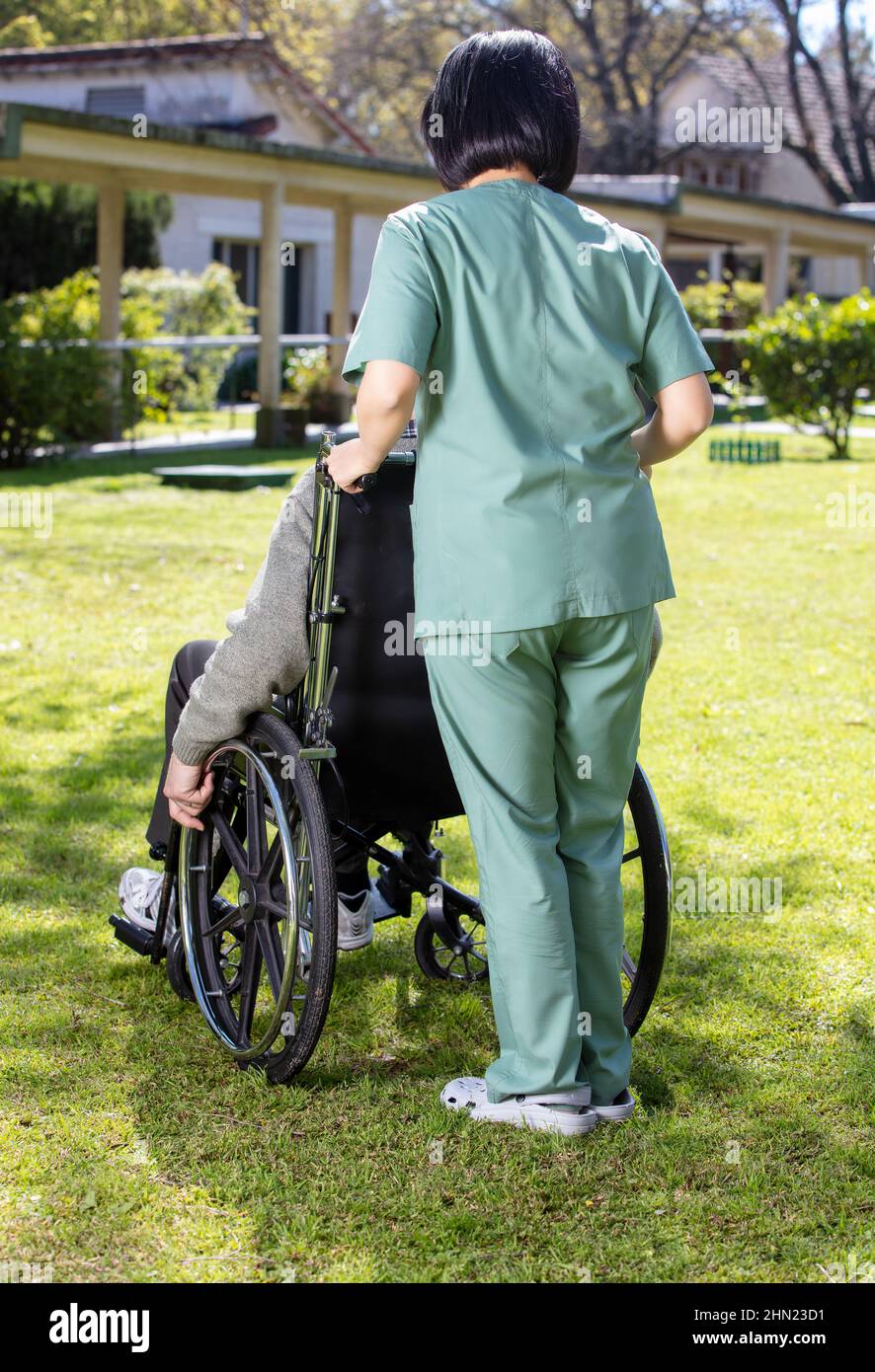Caucasian senior on the wheelchair helped by nurse outdoor. Retired elderly people living their life at its best Stock Photo