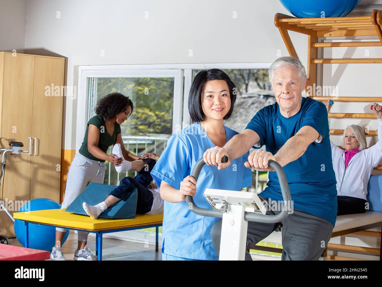 Happy couple of seniors smiling training at the gym helped by asian and ...