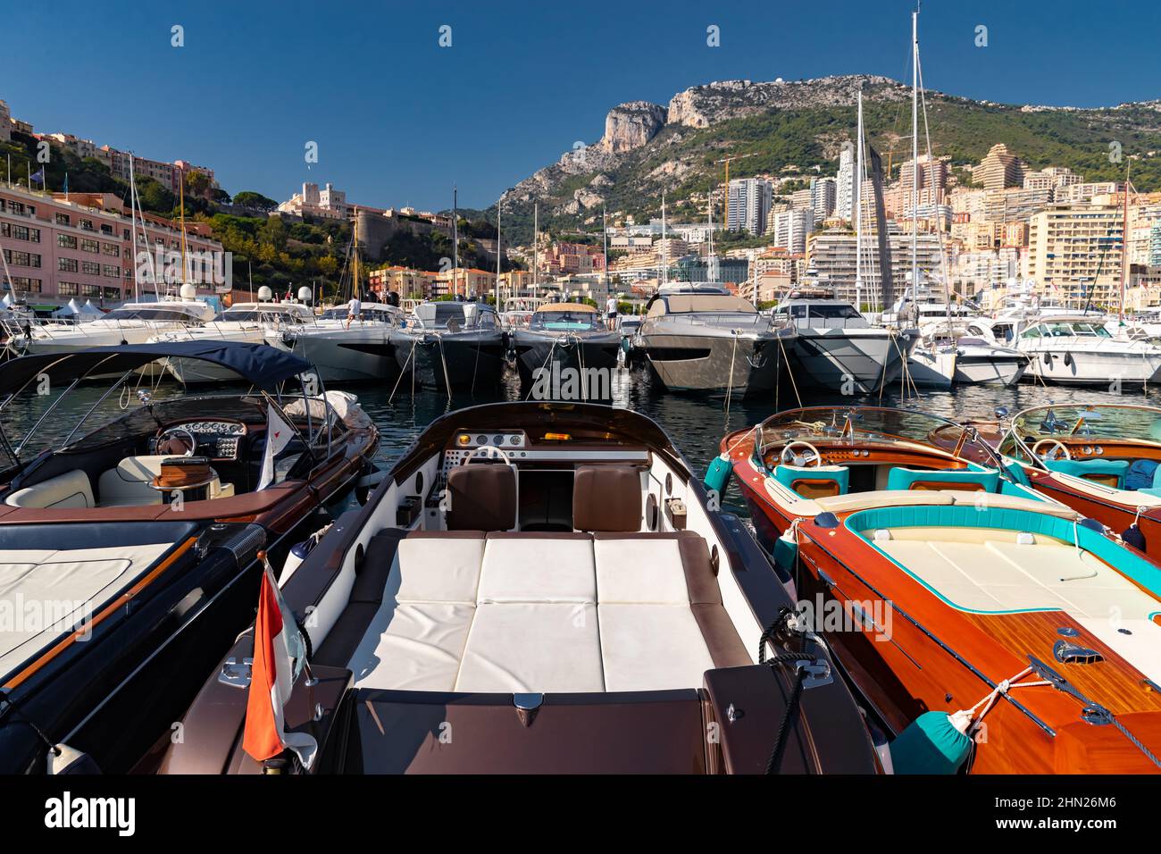 A lot of motor boats in rows are in port of Monaco at sunny day, Monte Carlo, mountain is on background, colourful interior of the boat, are moored in Stock Photo