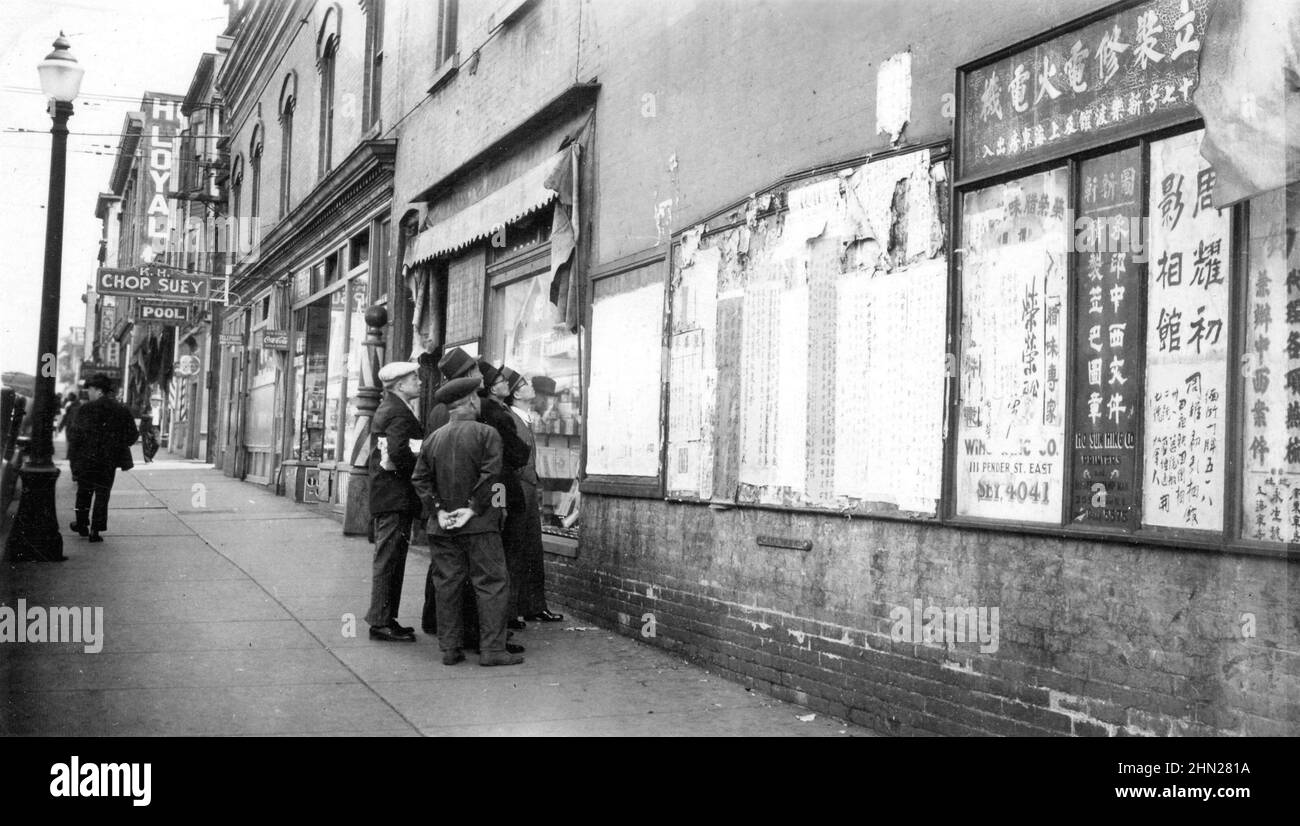 Vintage black and white photograph ca, 1936 of Chinese men reading newspapers posted on the wall of a building in Chinatown,  Vancouver, British Columbia, Canada Stock Photo